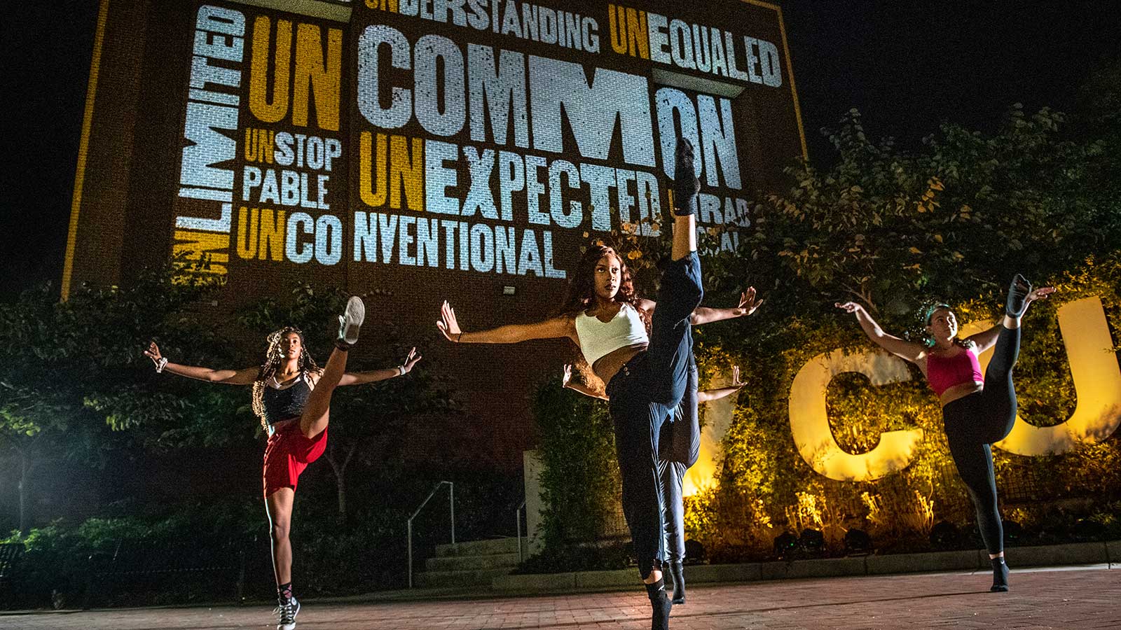 three v.c.u. dancers performing high kicks during an outdoor dance performance