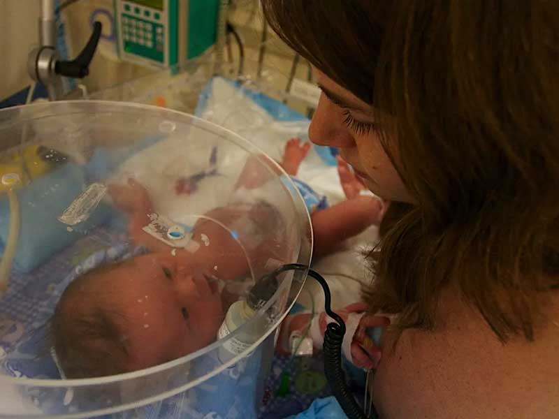 A new mother looking at a baby lying in an incubator at a hospital