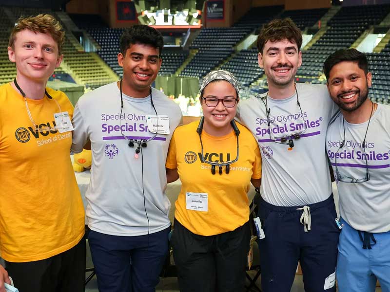 four v.c.u. volunteers with v.c.u. school of dentistry and special olympics shirts pose for a group photo in the siegel center at v.c.u.